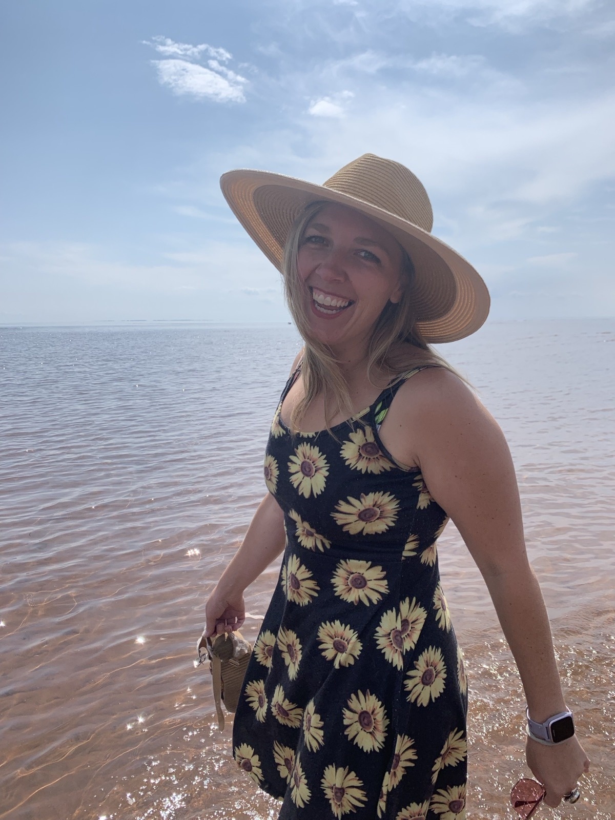 Amber Campbell smiling at the beach in a sun hat and sunflower-print sundress