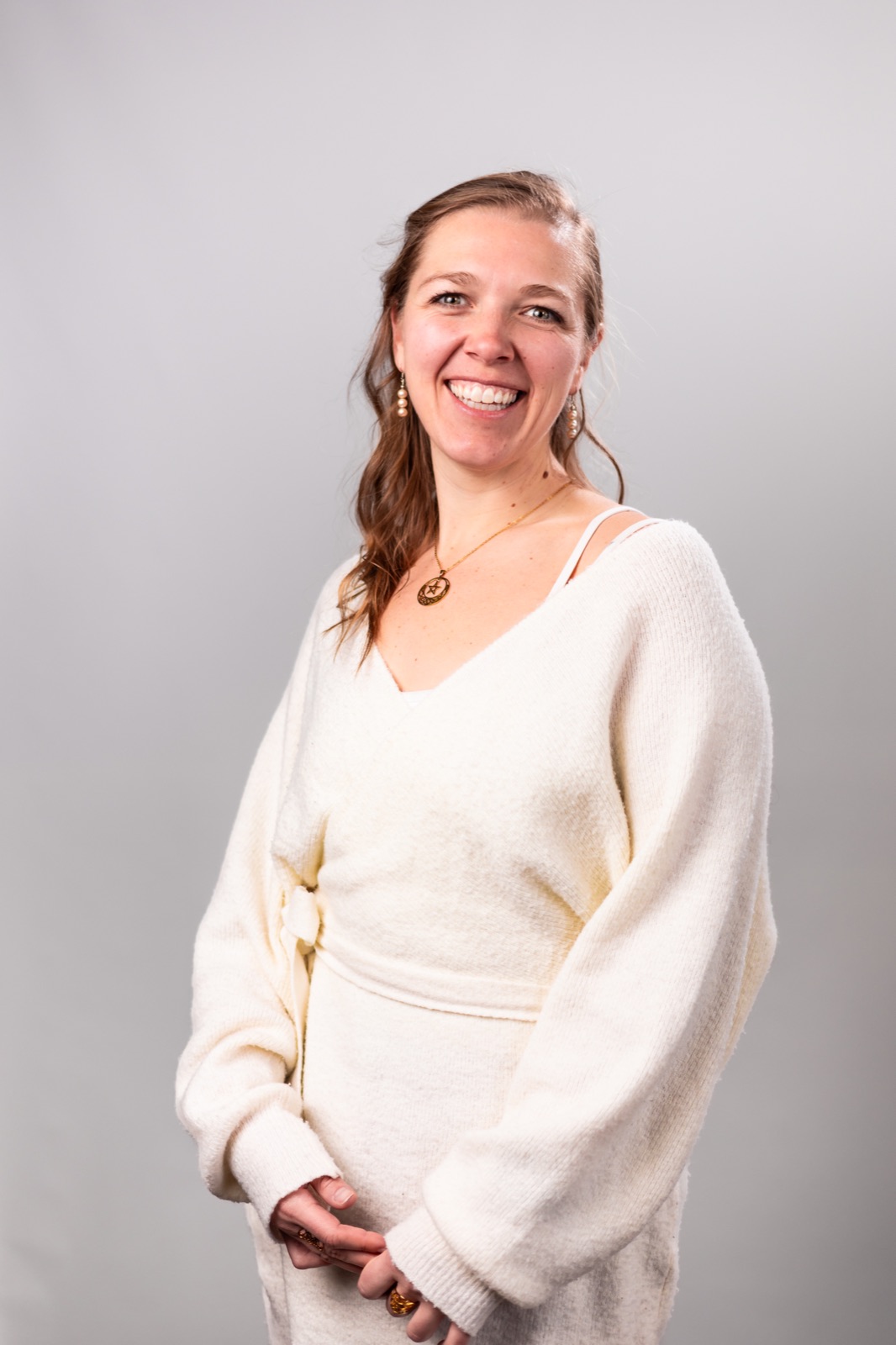 Amber Campbell standing in a cream sweater against a soft grey studio background