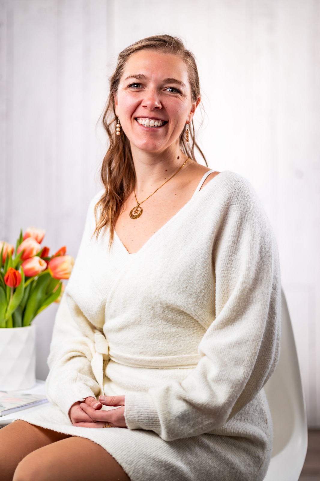 Amber Campbell smiling warmly while seated beside a bouquet of orange and pink tulips